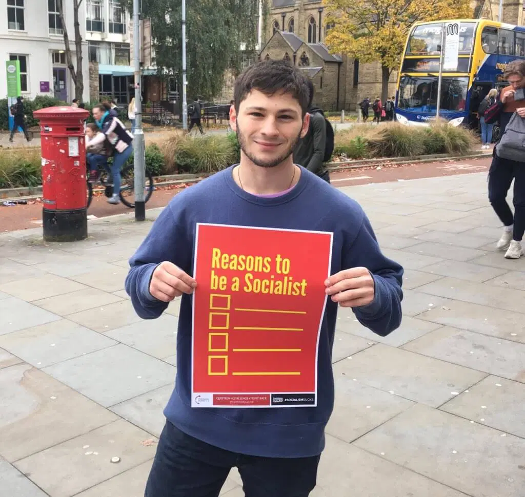 Young man holding a 'Reasons to be a Socialist' flyer at a Turning Point UK street stall.