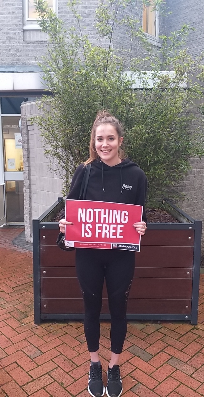Young woman holding a red 'NOTHING IS FREE' protest sign at a Turning Point UK action.