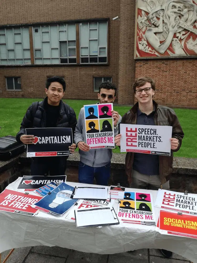 Three men behind a table with signs at a Turning Point UK Coventry stall.