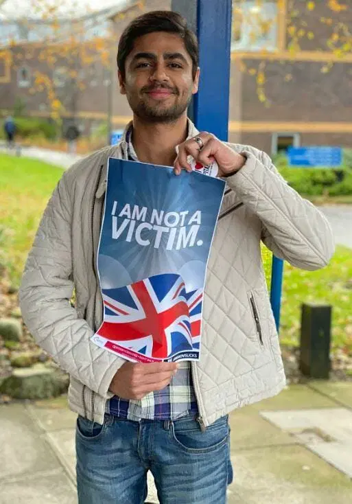 Man holding an I AM NOT A VICTIM poster at a Turning Point UK stall.