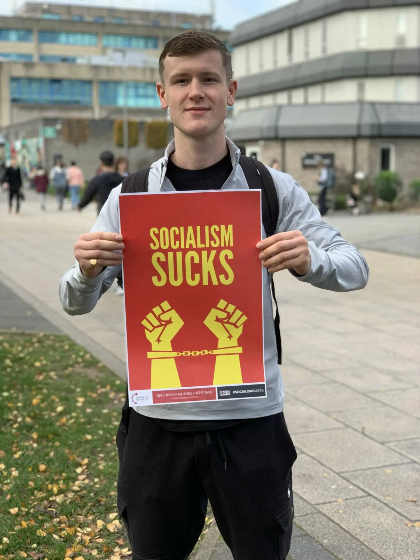 Man holding a 'SOCIALISM SUCKS' poster at a Turning Point UK stall.
