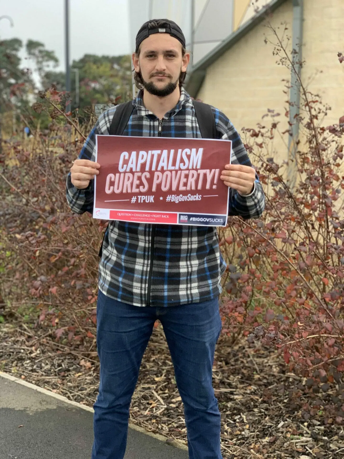 Man holding a CAPITALISM CURES POVERTY sign at a Turning Point UK event.