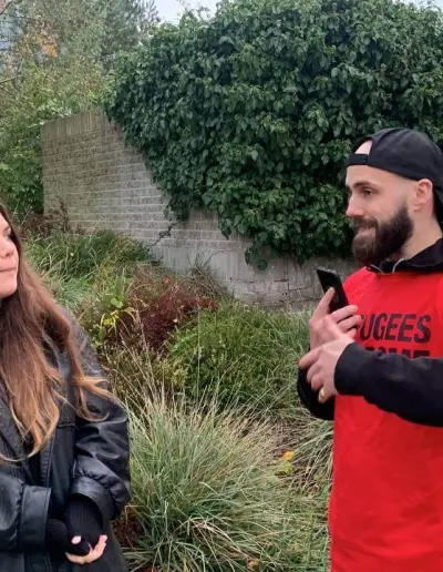 Two people outdoors, one wearing a Refugees Welcome shirt.