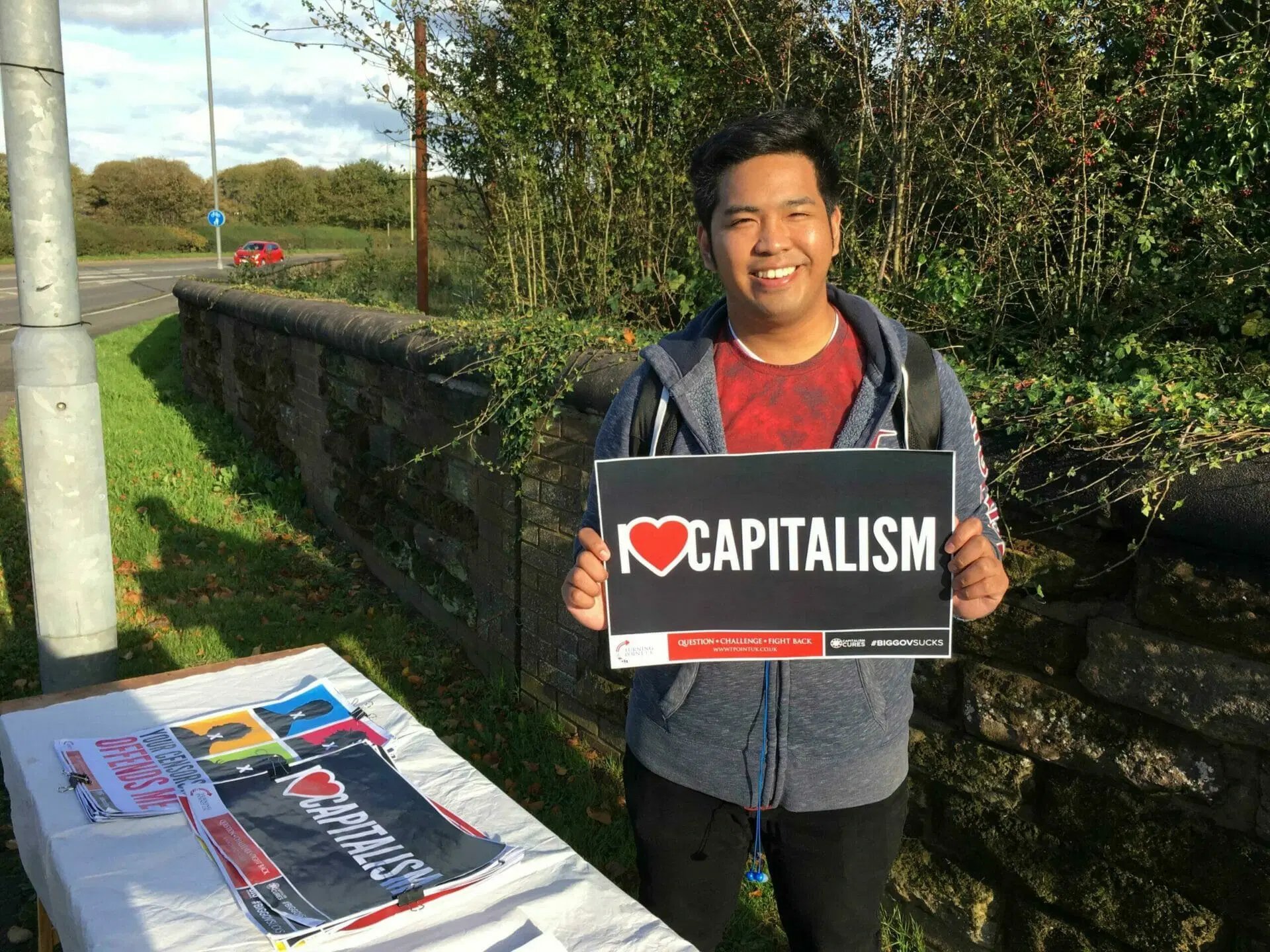 TPUK activist holding an I LOVE CAPITALISM sign at a campus stall.