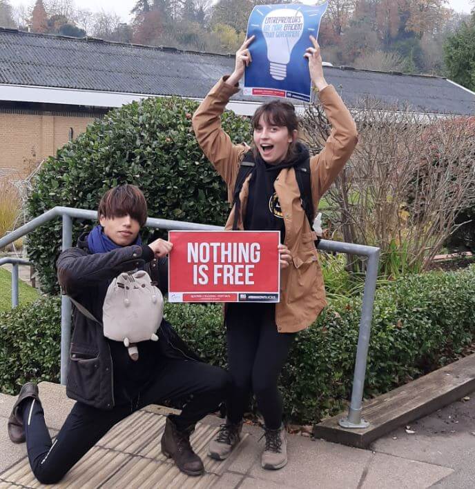 Two TPUK activists holding a NOTHING IS FREE sign and a flyer.